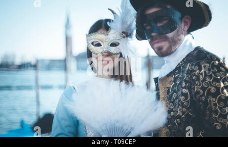 Couple of masks at the Venice carnival standing on the pier of the lagoon Stock Photo