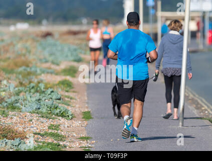 Man jogging by the roadside with sweat covering his shirt in Summer in the UK. Male jogger sweating, perspiring, back covered in perspiration. Stock Photo