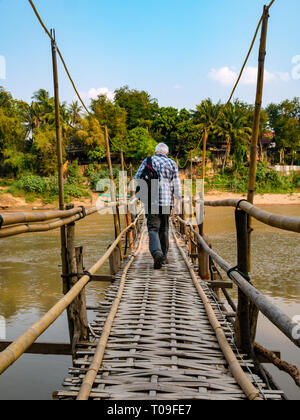Senior male tourist walking across rickety bamboo cane bridge over Nam Kahn river tributary of Mekong, Luang Prabang, Laos, Indochina, SE Asia Stock Photo
