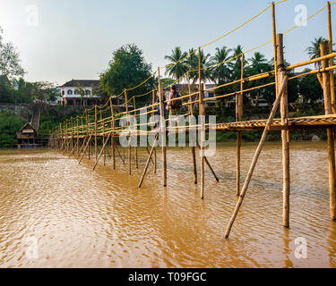 Girls walking across rickety bamboo cane bridge over Nam Kahn river tributary of Mekong, Luang Prabang, Laos, Indochina, SE Asia Stock Photo