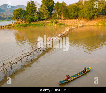 Boys walking on rickety bamboo cane bridge with girls in dugout canoe, Nam Kahn river tributary of Mekong, Luang Prabang, Laos, Indochina, SE Asia Stock Photo