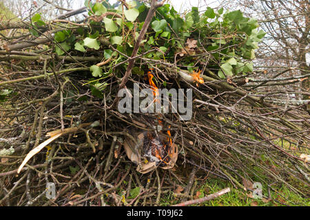 Setting fire with paper and cardboard to light a domestic bonfire to burn leaves, tree branches & twigs, lit in a domestic garden in the countryside. (104) Stock Photo