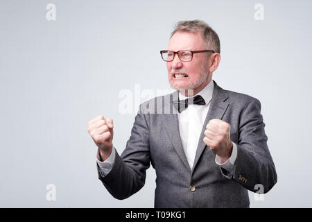 Handsome elegant senior man angry and mad raising fist up Stock Photo