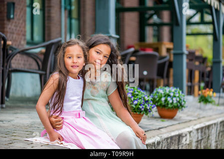 two beautiful asian sisters sitting on the sidewalk Stock Photo
