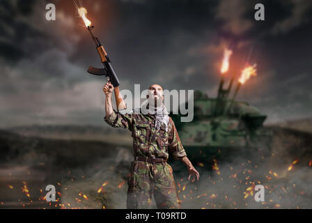Bearded terrorist with rifle in hands stands in explosion and fire. Terrorism and terror, soldier in khaki camouflage Stock Photo