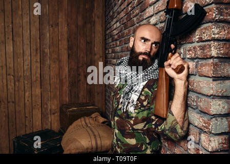 Terrorist in uniform with kalashnikov rifle hiding behind a wall, male mojahed with weapon. Terrorism and terror, soldier in khaki camouflage, boxes o Stock Photo