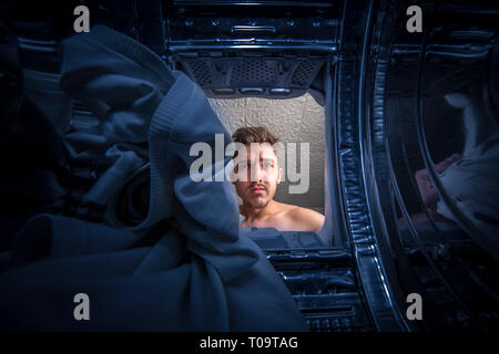 Young man doing laundry View from the inside of broken washing machine Stock Photo