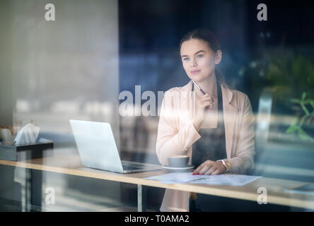 Woman working on laptop at coffee shop. Window Reflexions. Shot of a young woman using a laptop in a cafe Stock Photo