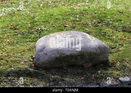 A large round stone lies in the park on the grass. Stock Photo