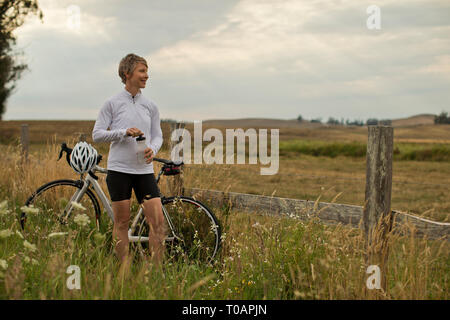 Smiling mature woman taking a break from bike riding to admire a rural field. Stock Photo