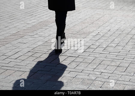 Silhouette of lonely woman walking down the street, black shadow on pavement. Slim female legs outdoor, concept of loneliness, diet, dramatic life sto Stock Photo