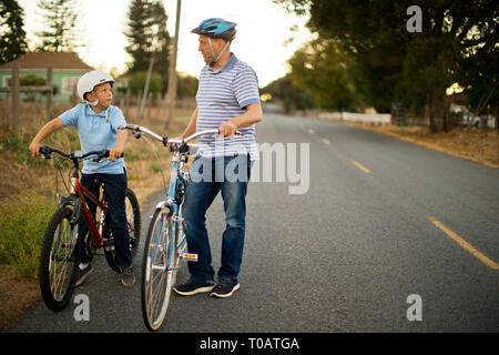 Happy father and son riding bikes along a country road. Stock Photo