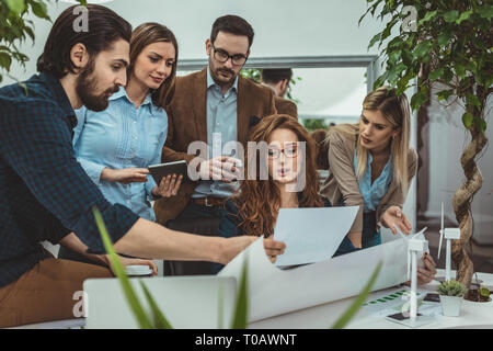 Smart qualified skilled young engineers are looking at the project of alternative energy with miniatures of windmill turbines at the table. Stock Photo
