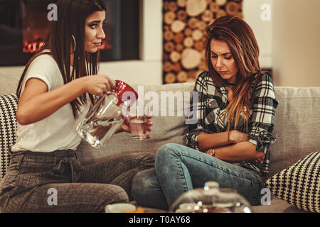 Two women sit in the room and talk. One complains that she has stomach ache, and another pours a glass of water to her. Stock Photo