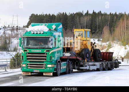 Salo, Finland - March 9, 2019: Green Scania truck with Noteboom low loader trailer carrying old wheel loader ready for transport on a day of winter. Stock Photo