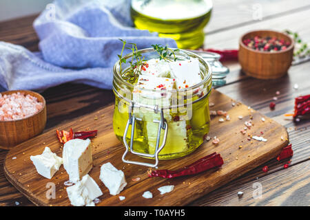 Feta cheese marinated in olive oil with fresh herbs in glass jar. Wooden background. Stock Photo