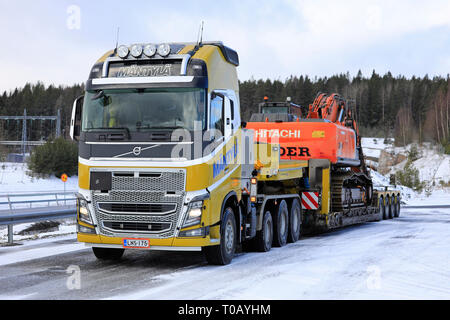 Salo, Finland - March 9, 2019: Volvo FH16 truck Mantyla with low loader trailer carrying Hitachi ZX 350LC excavator as wide load on a day of winter. Stock Photo