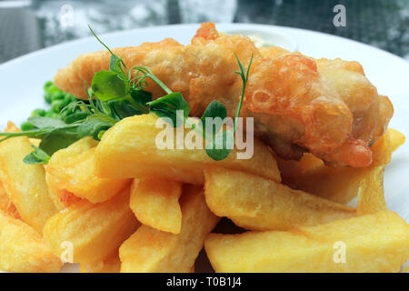 Traditional English food of cod fish and chips,  garnished with greens, served on a white plate. Stock Photo