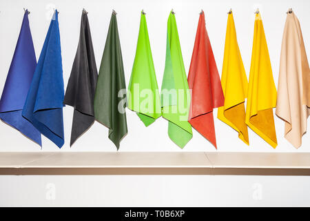 Pieces of leather material for example in the catalog of different colors for the design studio suspended on hooks in a textile workshop Stock Photo