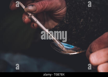 A female heroin addict draws freshly cooked heroin into a syringe. Stock Photo