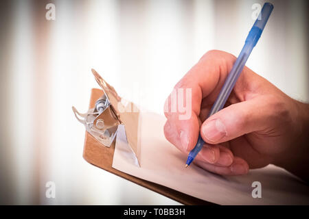 Hand holding blue pen to write checklist, contract, or concept on paper and clipboard Stock Photo