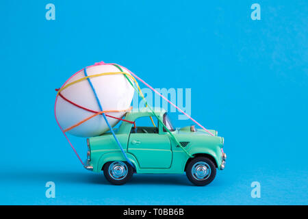 Car toy carrying easter egg tied with colorful thread minimal creative holiday and travel concepts. Stock Photo