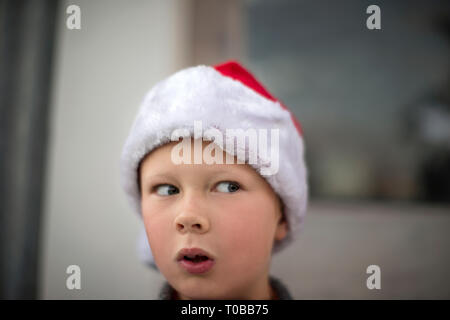 Young boy wearing a santa hat looks suspiciously sideways. Stock Photo