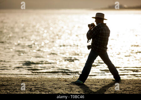 Mature photographer takes photographs on the beach at sunset. Stock Photo