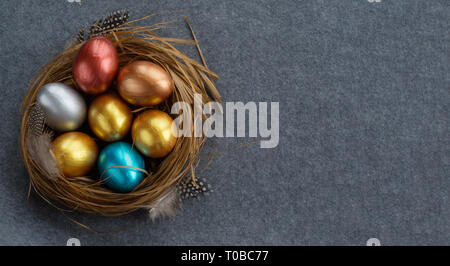 Happy Easter holiday greeting symbol stylish natural wooden grass nest with colorful quail eggs and feathers on gray fabric background Stock Photo