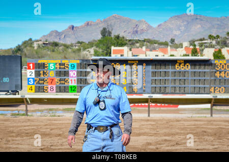 A mustached man wearing a cowboy hat is working Security at the Rillito Park Racetrack standing in front of the tote board in Tucson, AZ Stock Photo