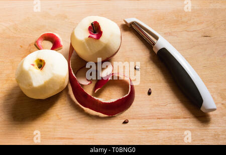 Red Apples peeled on a wood plank. Twisted peels, apple seeds and peeler Stock Photo