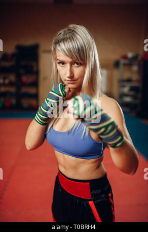 Female kickboxer in boxing bandages and sportswear, practicing hand punch with male personal trainer in pads, workout in gym. Woman boxer on training, Stock Photo
