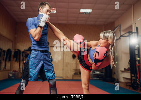Female kickboxer practicing kicking with male personal trainer, workout in gym. Boxer strikes on training, kickboxing practice Stock Photo
