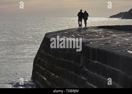 Silhouettes of people walking on the harbour wall, known as The Cobb, at Lyme Regis, Dorset, Great Britain. Stock Photo