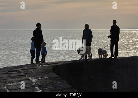 Silhouettes of people walking on the harbour wall, known as The Cobb, at Lyme Regis, Dorset, Great Britain. Stock Photo