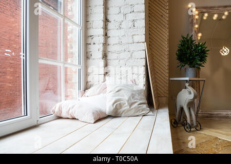 Bright studio interior with big window, high ceiling, wooden floor.Loft style bedroom interior design. Beige pillows and brick wall. scandinavian Stock Photo