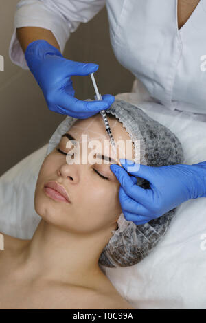 Aesthetic cosmetology. Facelift in spa salon. Beautician doing injection girl's brow creases. Smoothing facial wrinkles. Close-ups Stock Photo