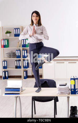 Young female employee doing exercises at workplace Stock Photo