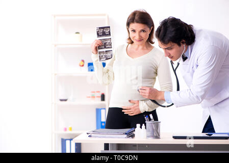 Old pregnant woman visiting young male doctor Stock Photo