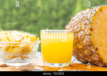 Sliced pineapple kept on a wooden table besides a glass filled with pineapple juice and a glass bowl with pineapple slices Stock Photo