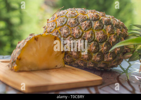 A quarter slice of a ripe pineapple kept vertically on a table outdoors with a whole pineapple with leaves Stock Photo
