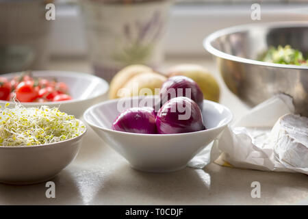 Spring salad ingredients: red onion, tomatoes, mixed leaves lettuce, pears, sprouts, brie on kitchen table Stock Photo