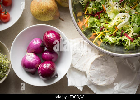 Spring salad ingredients: red onion, tomatoes, mixed leaves lettuce, pears, sprouts, brie on kitchen table Stock Photo