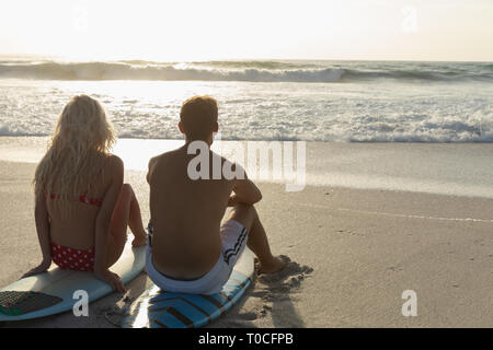 Happpy Caucasian couple relaxing on surf board at beach Stock Photo