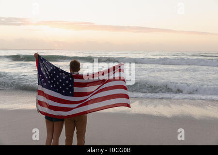 Young Caucasian couple holding american flag at beach Stock Photo