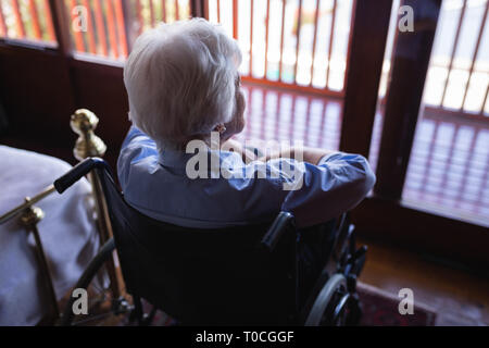 Disabled active senior woman sitting on wheelchair looking through window in bedroom at home Stock Photo