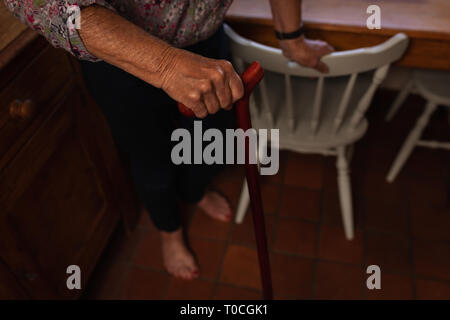 Active senior woman walking with cane in kitchen at home Stock Photo