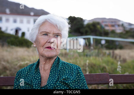 Thoughtful active senior woman sitting on wooden bench at sea Stock Photo