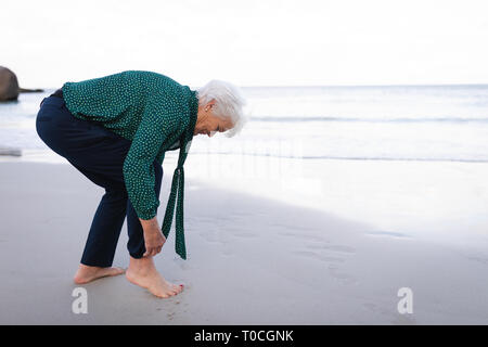 Active senior woman rolling up pant sleeves on the beach Stock Photo