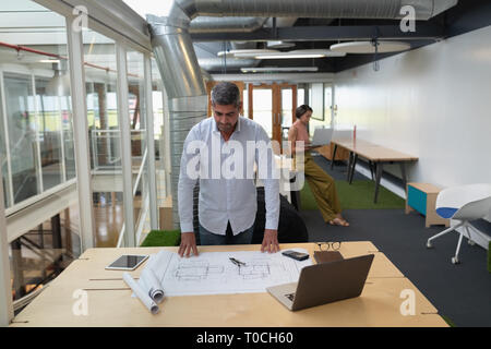 Man working at blueprint at desk in office Stock Photo